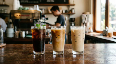 Three tall iced coffees on a wooden cafe counter showing the iced coffee shift in specialty cafe menu